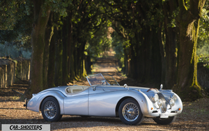 Jaguar XK 120 Retina – side profile, silver on a tree-lined dirt road