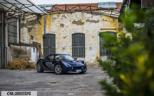 Lotus Elise WALLAPER1 Retina – front three-quarter, dark blue against an old industrial building