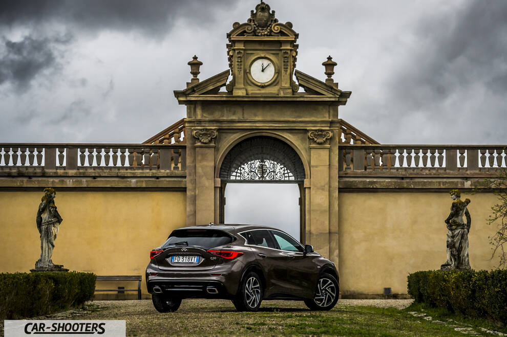 Infiniti Q30 – rear three-quarter, brown metallic against an old architectural backdrop