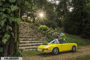 Porsche 911 Targa Storica – rear three-quarter, yellow against a stone stairway and park backdrop