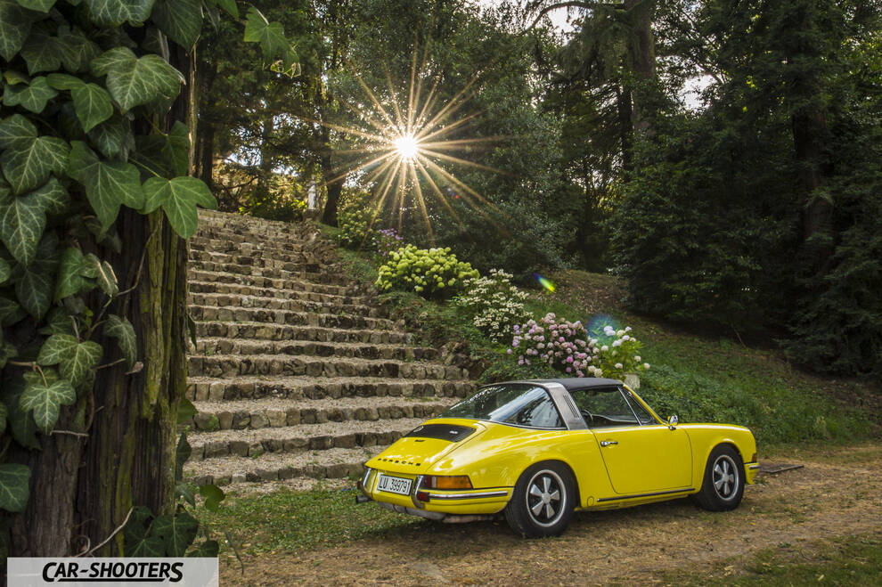 Porsche 911 Targa Storica – rear three-quarter, yellow against a stone stairway and park backdrop