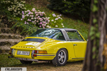 Porsche 911 Targa Storica – rear three-quarter, yellow against a garden backdrop