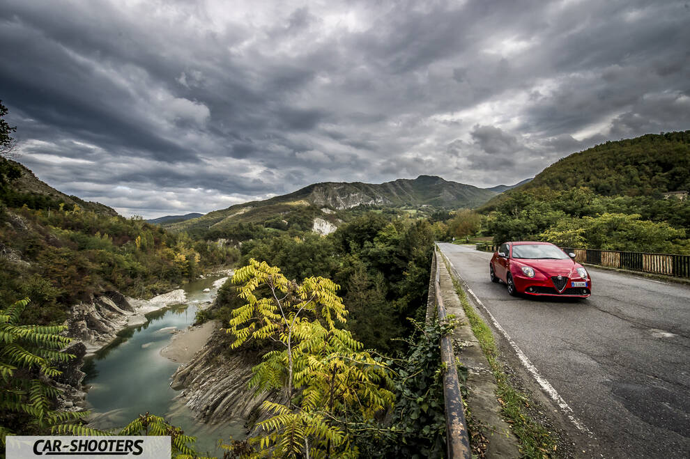 Alfa Romeo Mito Veloce Imola Mugello – front three-quarter, red on a road near a river and mountains