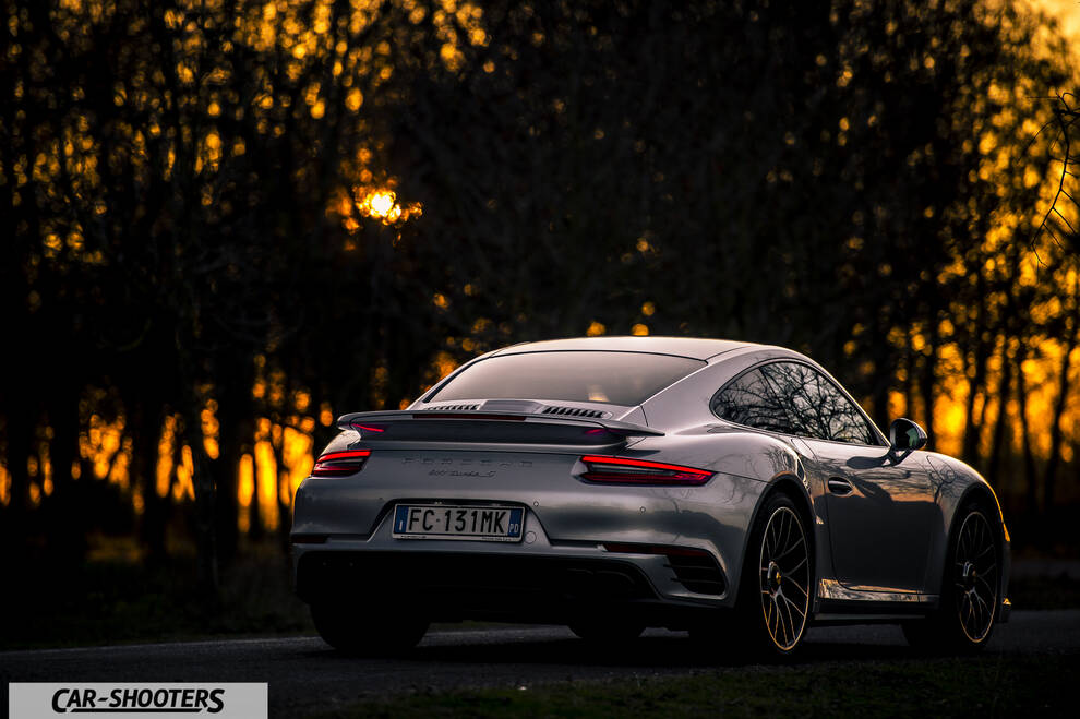Porsche 911 Turbo S – rear three-quarter, silver against a sunset tree backdrop