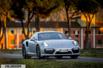 Porsche 911 Turbo S – front three-quarter, silver against a building backdrop