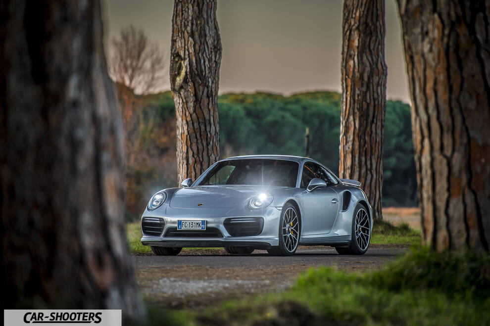 Porsche 911 Turbo S – front three-quarter, silver framed by tall pine trees