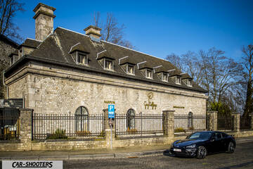 Toyota GT86 Namur – front three-quarter, black parked beside a stone building