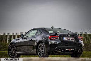 Toyota GT86 Namur – rear three-quarter, black against a wooden fence