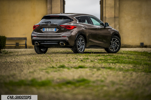 Infiniti Q30 – rear three-quarter, brown metallic against a rustic wall