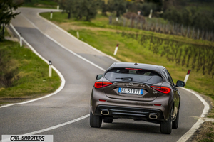 Infiniti Q30 – rear three-quarter, brown metallic on a winding country road