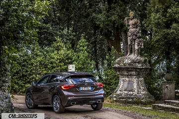 Infiniti Q30 – rear three-quarter, brown metallic on a dirt road near a statue