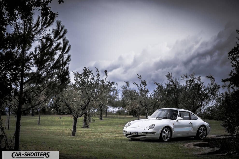 Porsche 993 Carrera 4 – front three-quarter, white on a grassy field with trees