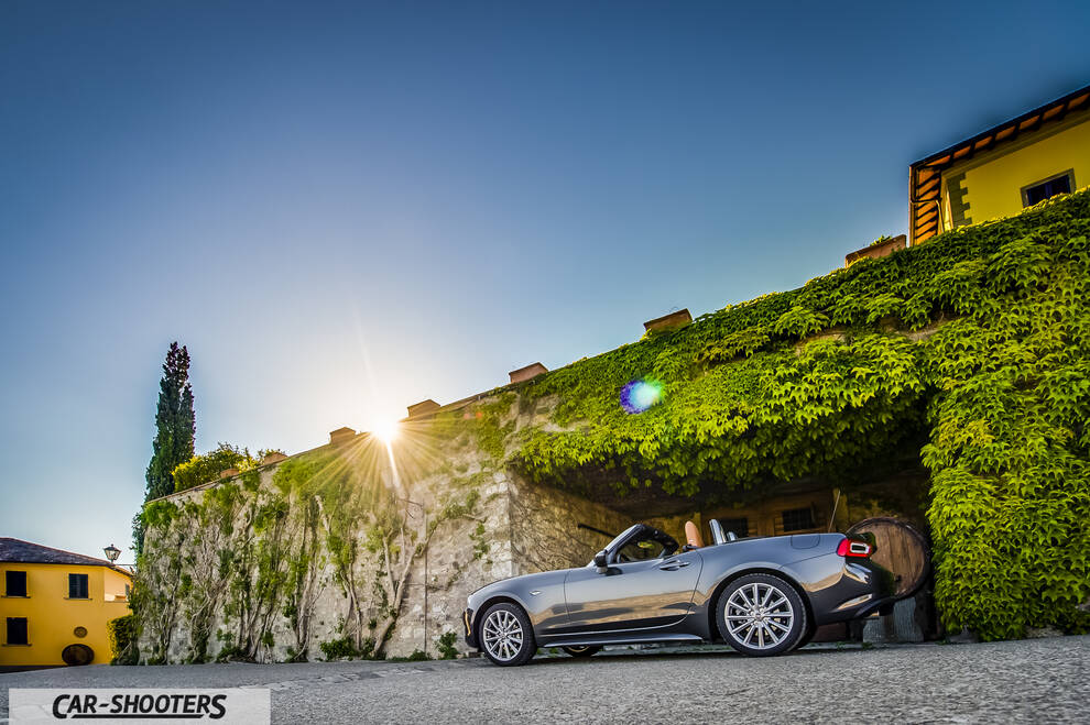 Fiat 124 Spider – rear three-quarter, grey metallic against a stone and vine wall