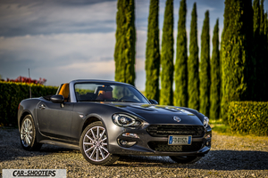 Fiat 124 Spider – front three-quarter, grey metallic against a cypress tree backdrop
