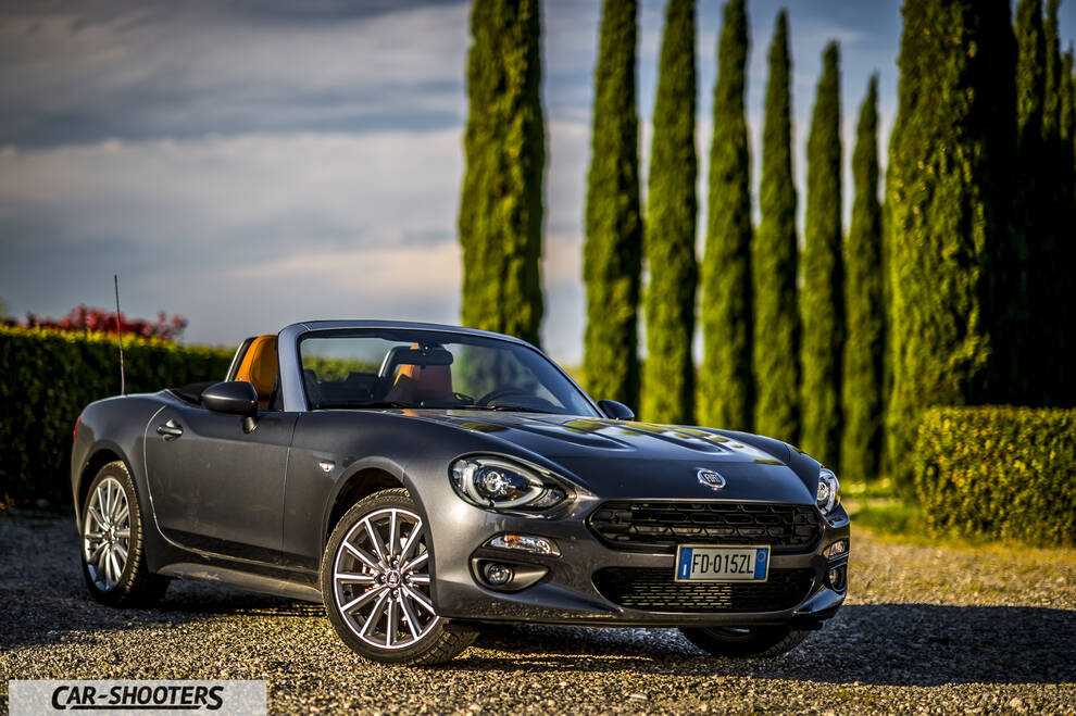 Fiat 124 Spider – front three-quarter, grey metallic against a cypress tree backdrop