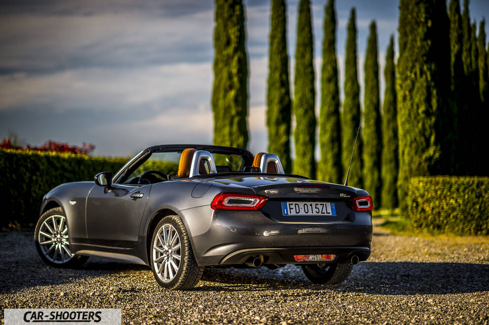 Fiat 124 Spider – rear three-quarter, grey metallic on a gravel driveway with cypress trees