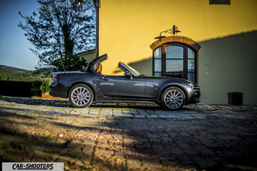 Fiat 124 Spider – side profile, grey metallic parked in front of a yellow building