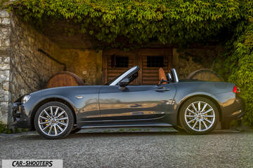 Fiat 124 Spider – side profile, grey metallic against an old stone wall
