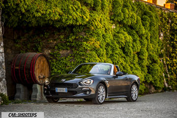 Fiat 124 Spider – front three-quarter, dark grey metallic against a stone wall with foliage