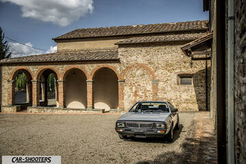Lancia Beta Montecarlo – front three-quarter, silver in front of a rustic building