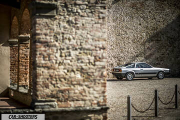 Lancia Beta Montecarlo – rear three-quarter, silver against an old stone wall