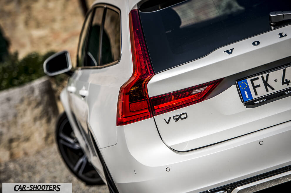 Volvo V90 T8 – rear three-quarter, white against a stone wall