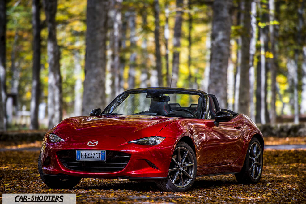 Mazda MX 5 ND – front three-quarter, red metallic against an autumn forest backdrop