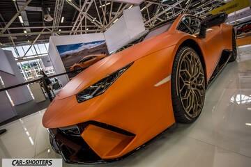 front three-quarter, matte orange at an indoor auto show