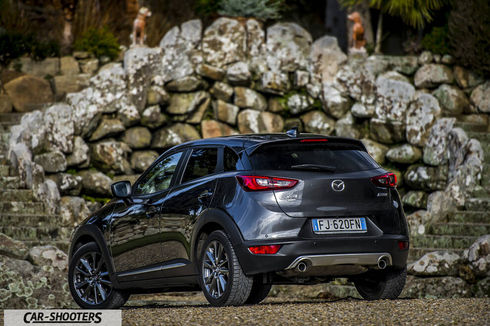 Mazda CX 3 – rear three-quarter, dark grey metallic against a stone wall backdrop