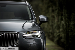Volvo XC90 – front three-quarter, grey metallic against a blurry hedge backdrop
