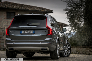 Volvo XC90 – rear three-quarter, grey metallic against a rural building backdrop