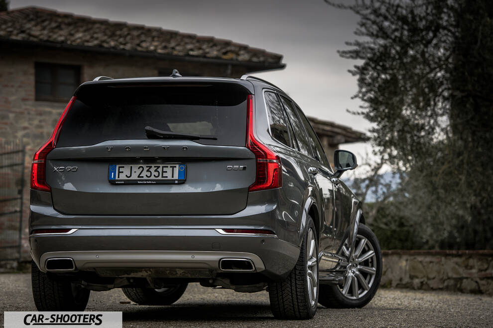 Volvo XC90 – rear three-quarter, grey metallic against a rural building backdrop