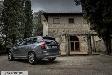 Volvo XC90 – rear three-quarter, grey metallic against a rustic building backdrop