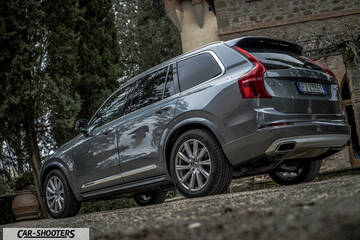 Volvo XC90 – rear three-quarter, grey metallic against a rustic building