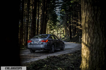 Infiniti Q50 – rear three-quarter, grey metallic on a road through forest
