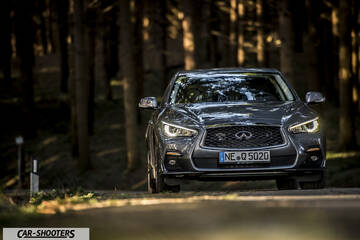 Infiniti Q50 – front three-quarter, grey metallic on a road through forest