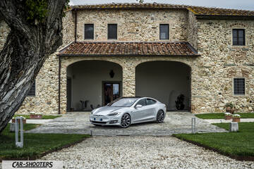 Tesla Model S – front three-quarter, silver parked in front of a rustic stone building