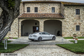 Tesla Model S – rear three-quarter, silver against a rustic stone building