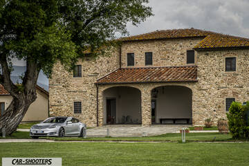 Tesla Model S – front three-quarter, silver metallic against a rustic stone building backdrop