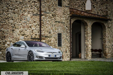 Tesla Model S – front three-quarter, silver metallic against a rustic stone building