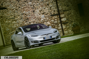Tesla Model S – front three-quarter, silver metallic against a rustic stone wall