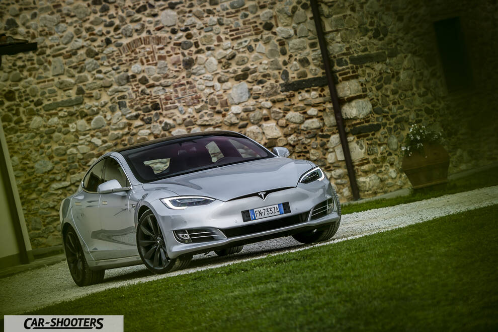 Tesla Model S – front three-quarter, silver metallic against a rustic stone wall