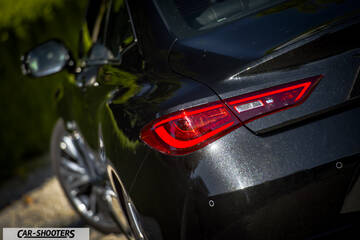 Infiniti Q60 – rear three-quarter, black against a leafy background