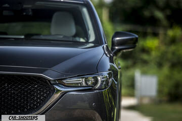 Mazda CX 5 – front three-quarter, dark grey metallic against a blurred green backdrop