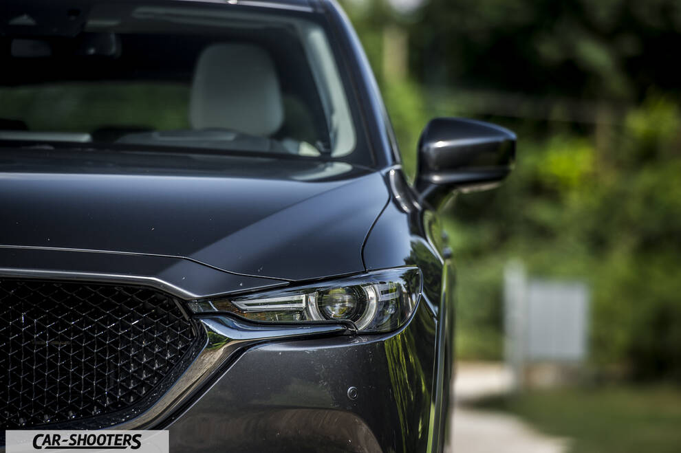 Mazda CX 5 – front three-quarter, dark grey metallic against a blurred green backdrop