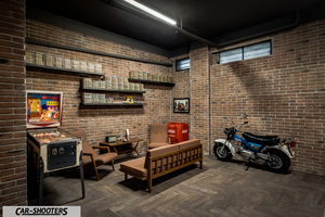 Porsche – side profile, white and blue in a brick room with a pinball machine