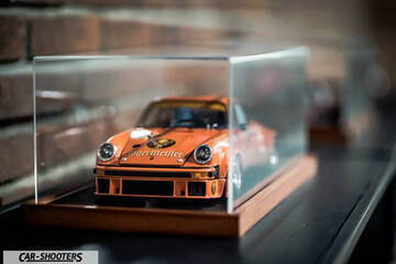 Porsche – front three-quarter, orange in a display case