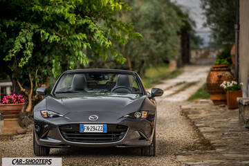 Mazda MX 5 Cherry Edition – front three-quarter, dark grey metallic on a rural path between foliage and a stone building