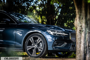 Volvo V60 – front three-quarter, dark blue metallic against a woodland backdrop