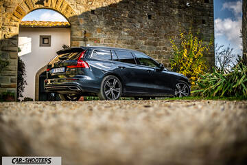 Volvo V60 – rear three-quarter, dark grey metallic in front of a stone building